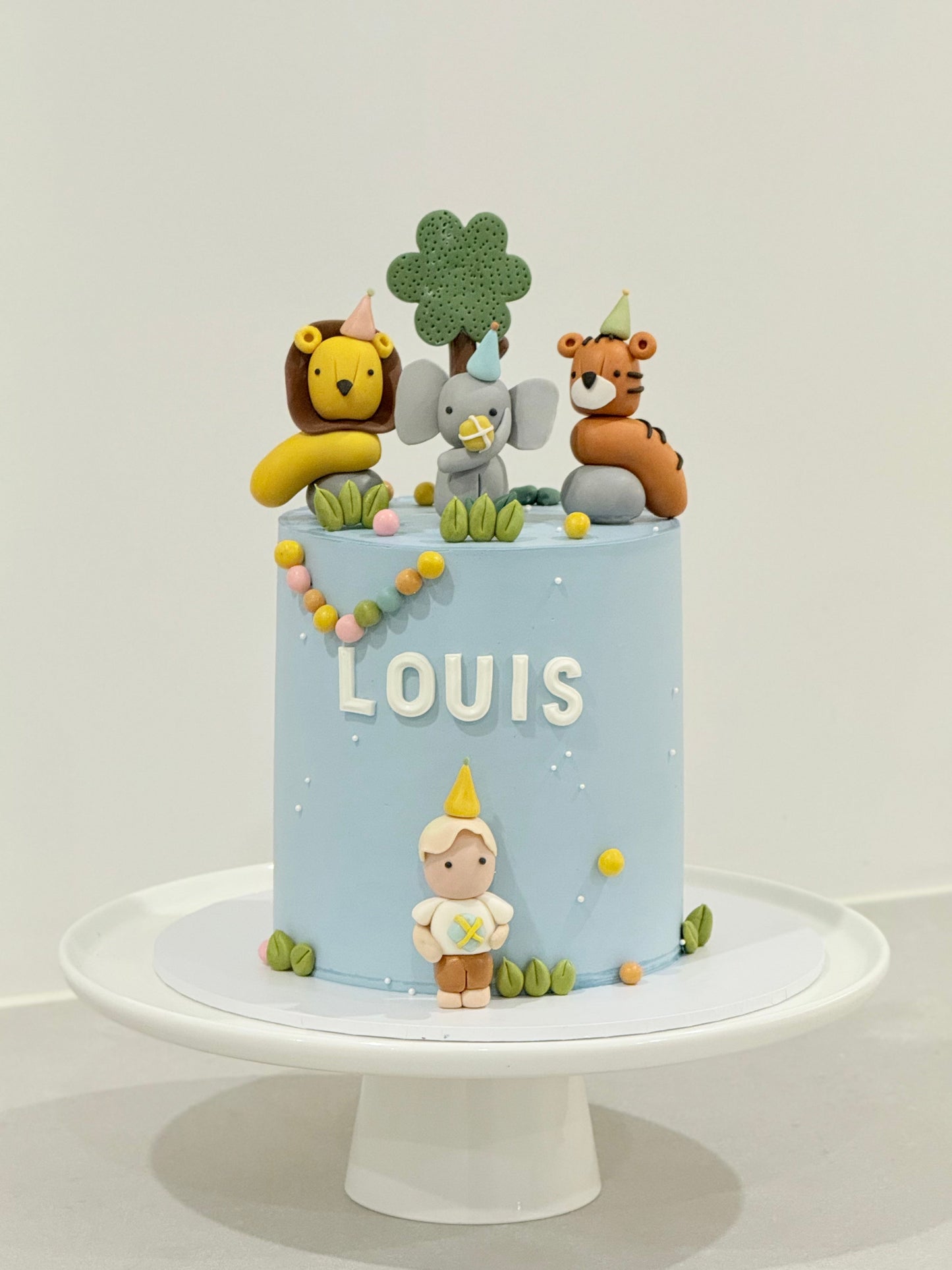 Cake with animal figurines and 'LOUIS' on a white background