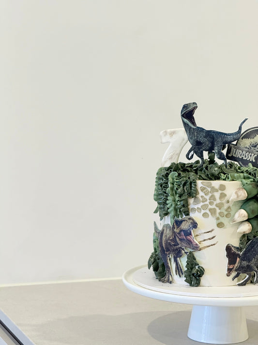 Blue Jurassic World kids birthday cake top view — dinosaur figurines and foliage detail — Bakeology Studios Melbourne