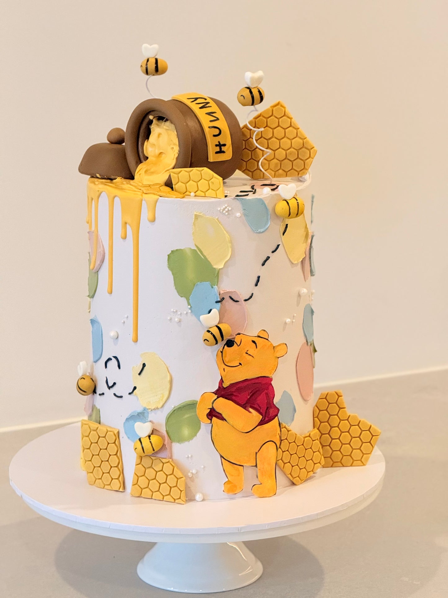 Cake with Winnie the Pooh and honeycomb decorations on a white stand.