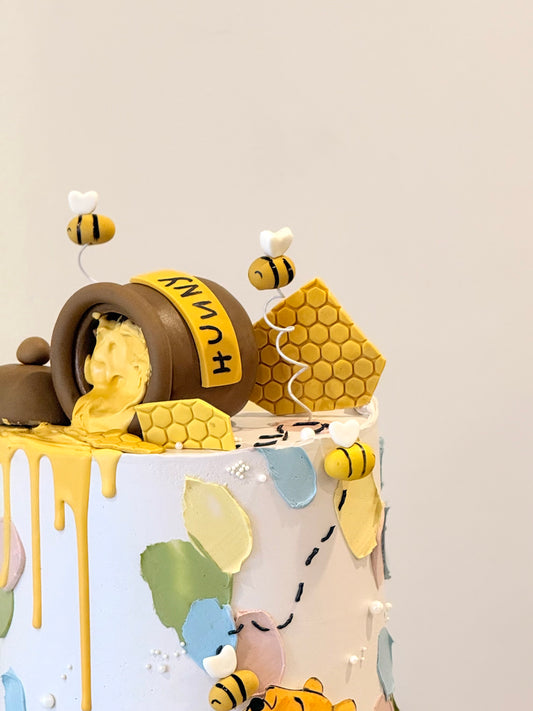 Children's birthday cake with honeycomb, bees, and a lion figure on a light gray background