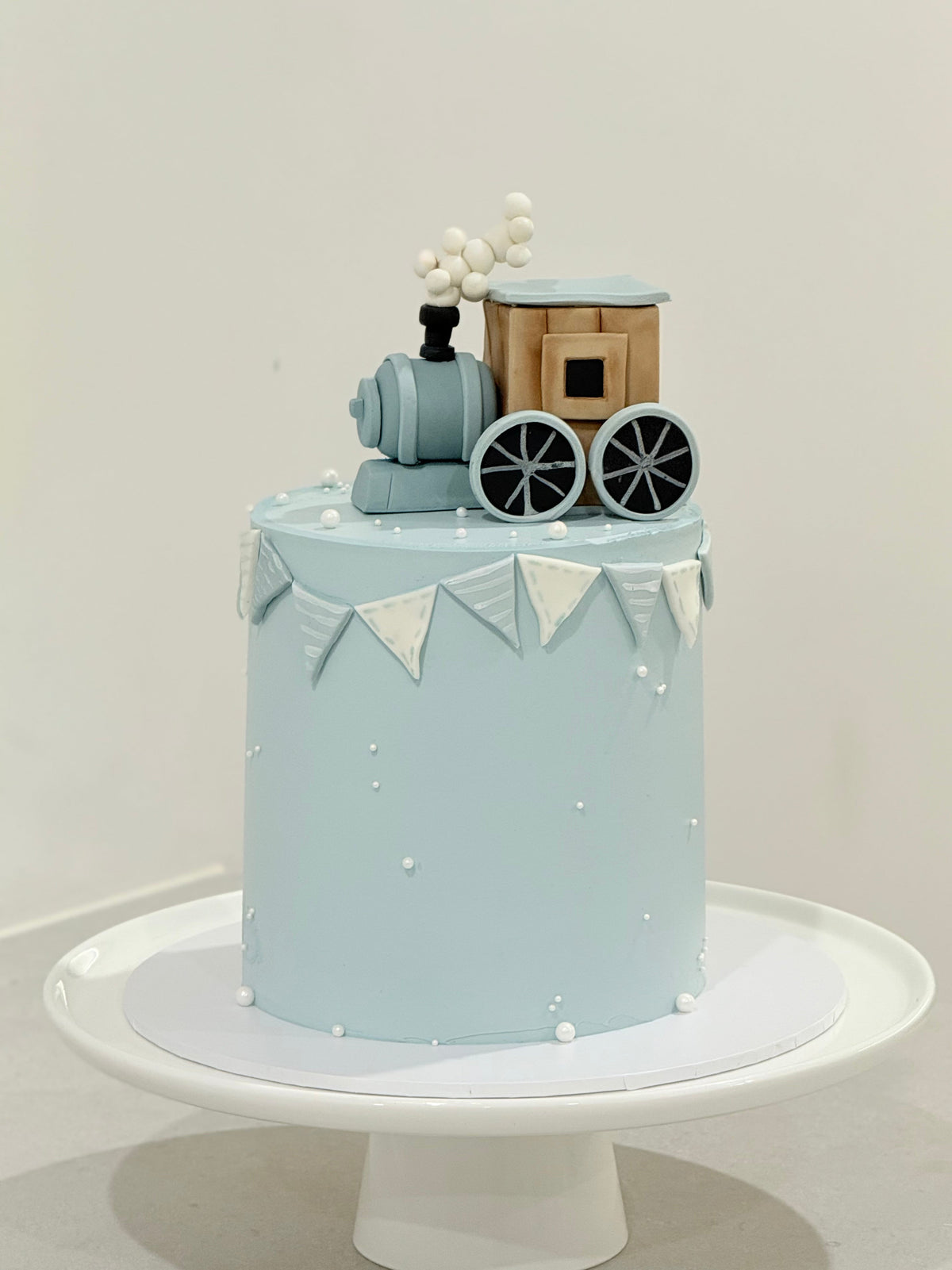 Xavier light blue train theme kids birthday cake on a white stand — Bakeology Studios Melbourne