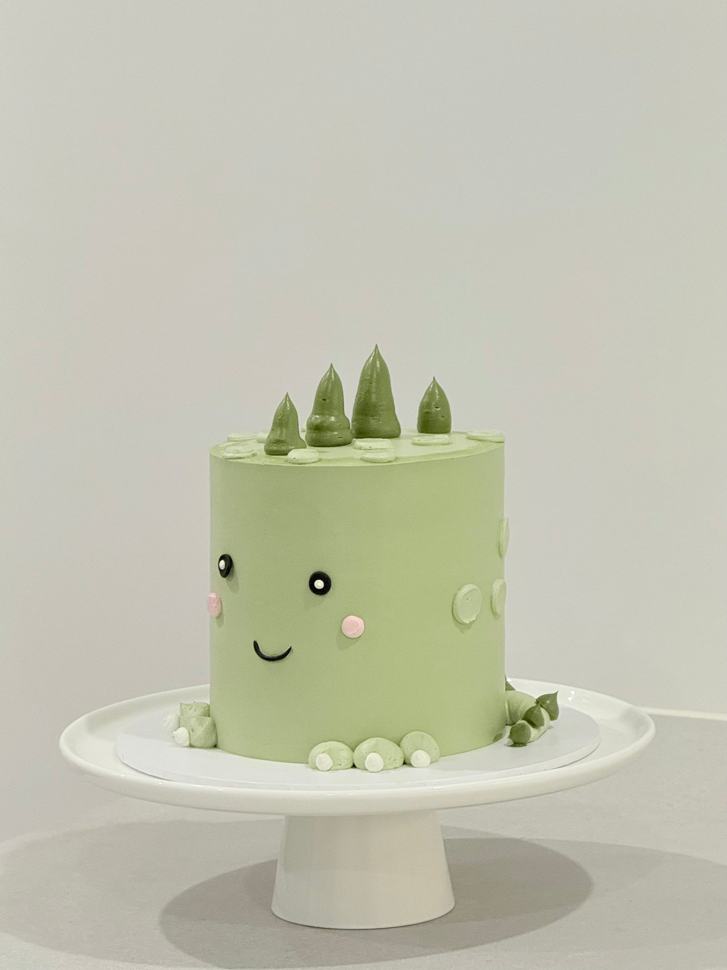 Dino style sage green smiley face kids birthday cake with pine tree toppers — Bakeology Studios Melbourne