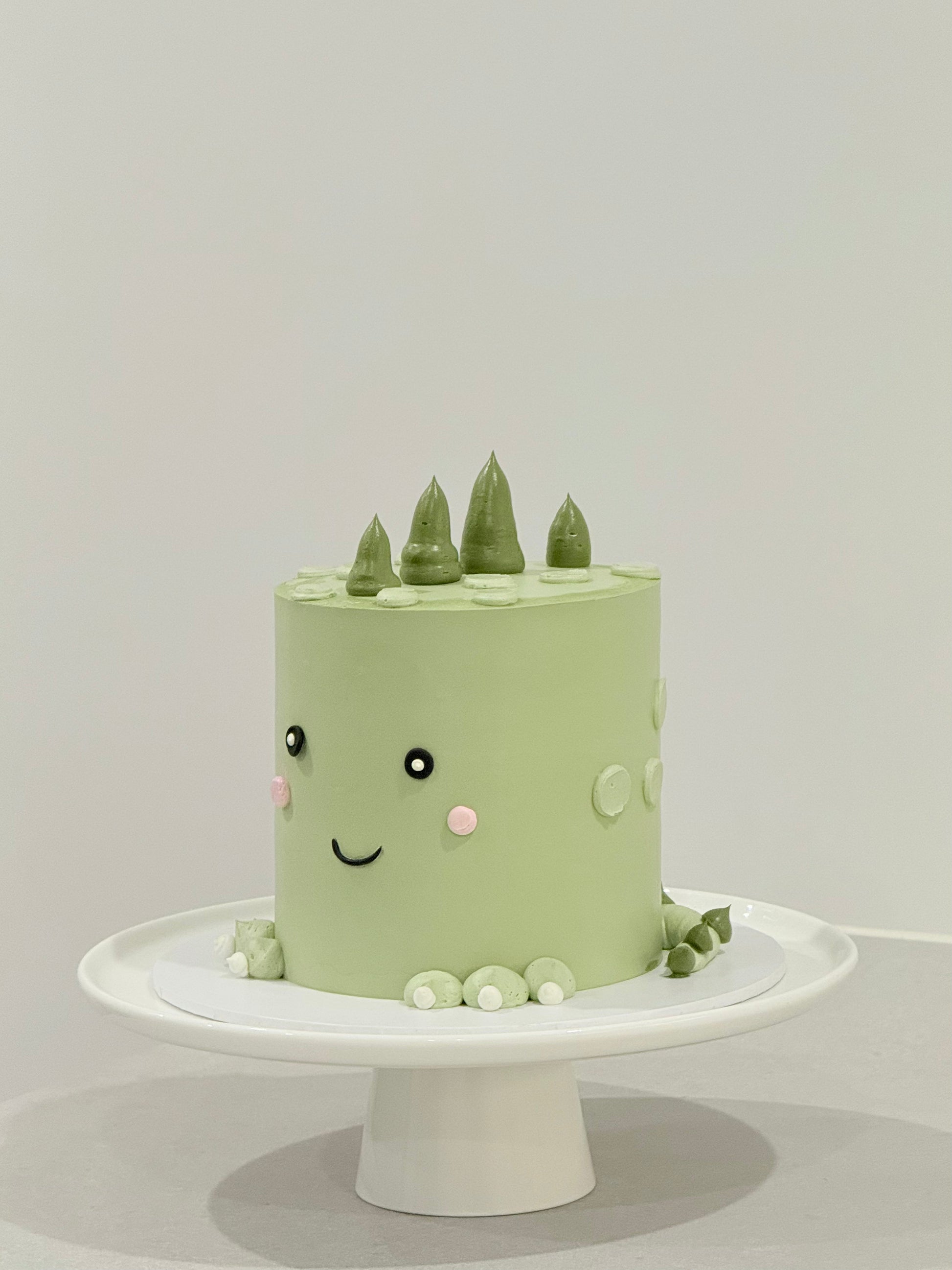 Dino style sage green smiley face kids birthday cake with pine tree toppers — Bakeology Studios Melbourne