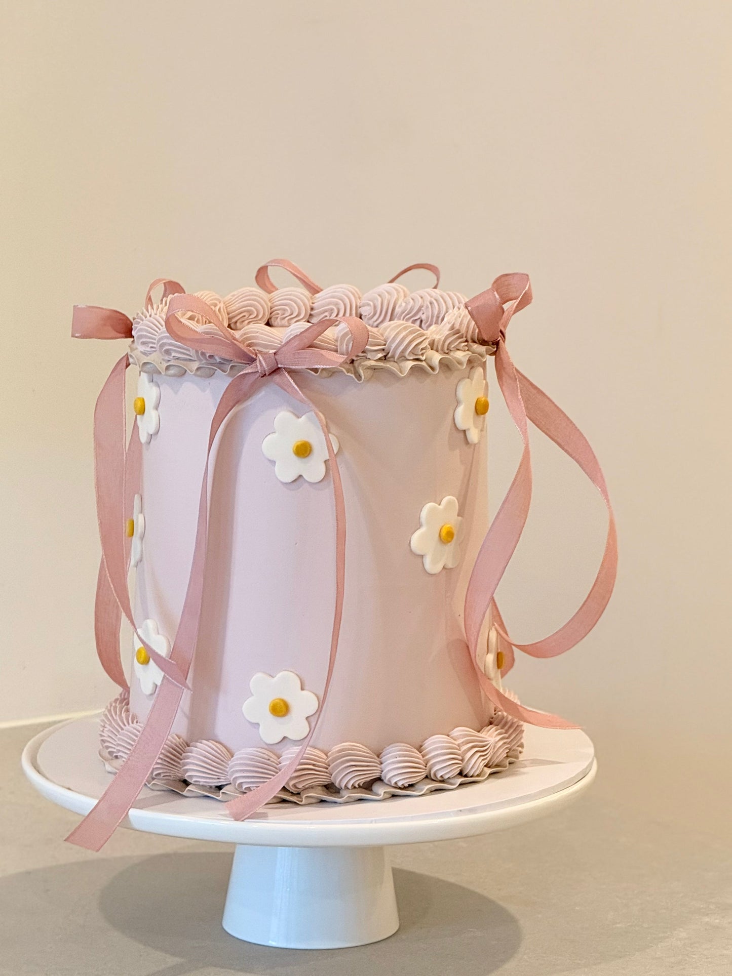 Decorative cake with pink ribbons and white flowers on a white stand against a light background