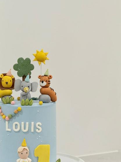 Children's birthday cake with animal toppers and 'LOUIS 1' text on a light gray background