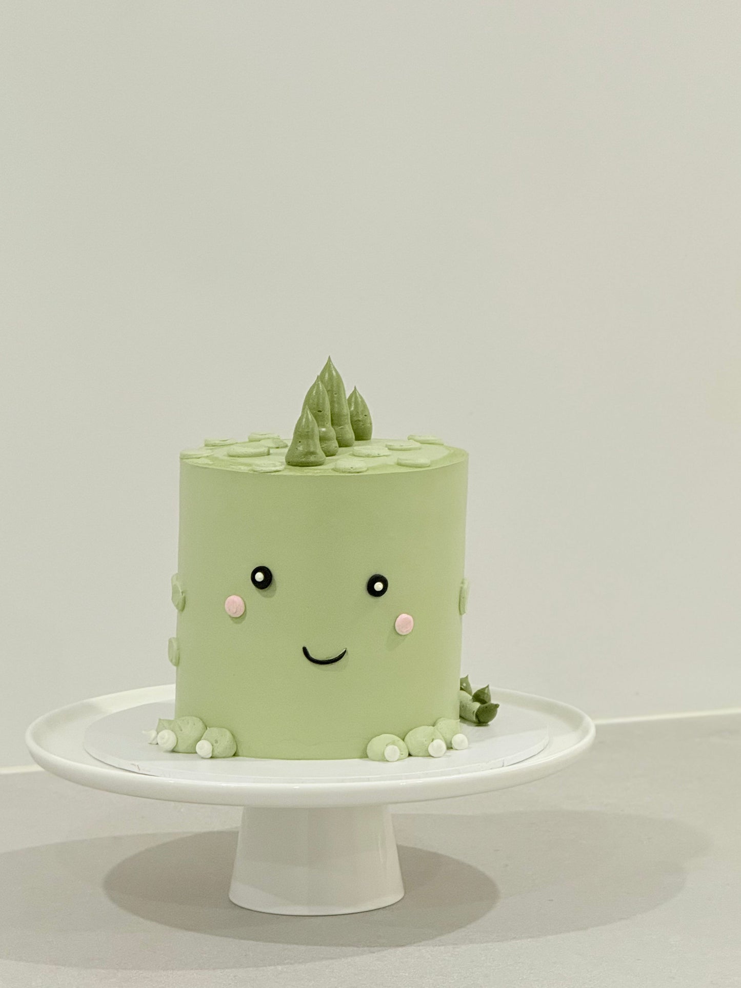 Handcrafted kawaii celebration cake sage green with smiley face topper — Bakeology Studios Burwood East