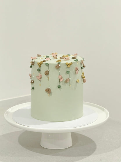 Light green cake with decorative elements on a white stand against a light gray background