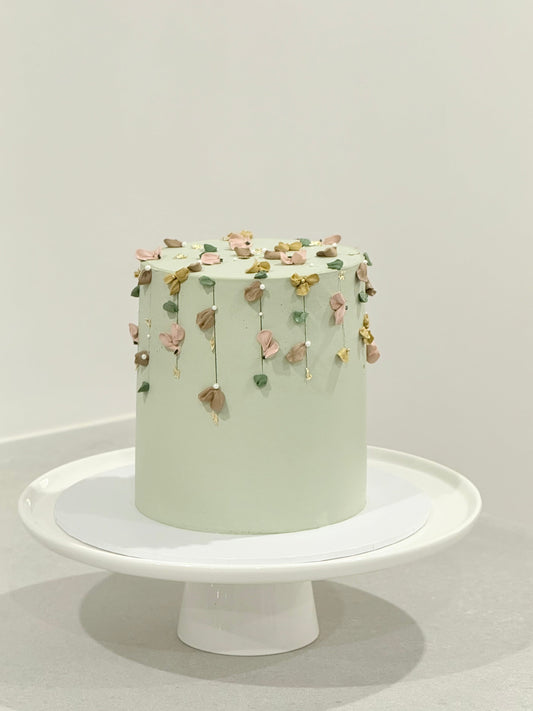 Light green cake with decorative elements on a white stand against a light gray background