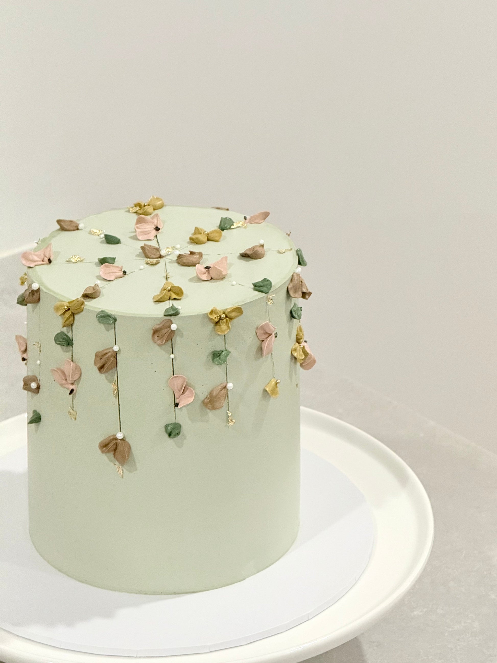 Light green cake with floral decorations on a white stand against a light gray background