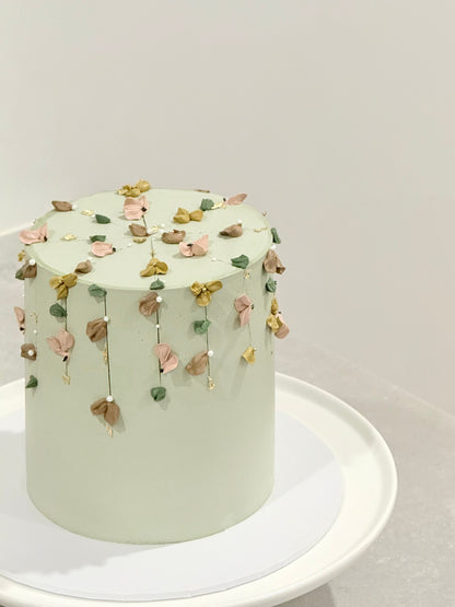 Light green cake with floral decorations on a white stand against a light gray background