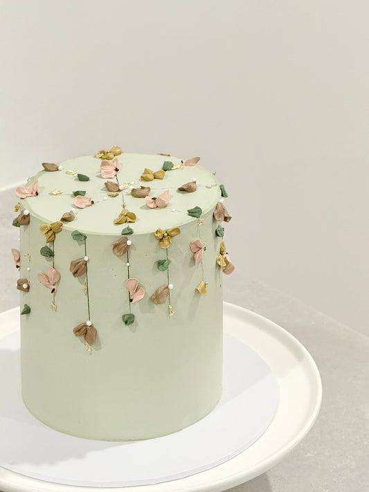 Light green cake with floral decorations on a white stand against a light gray background