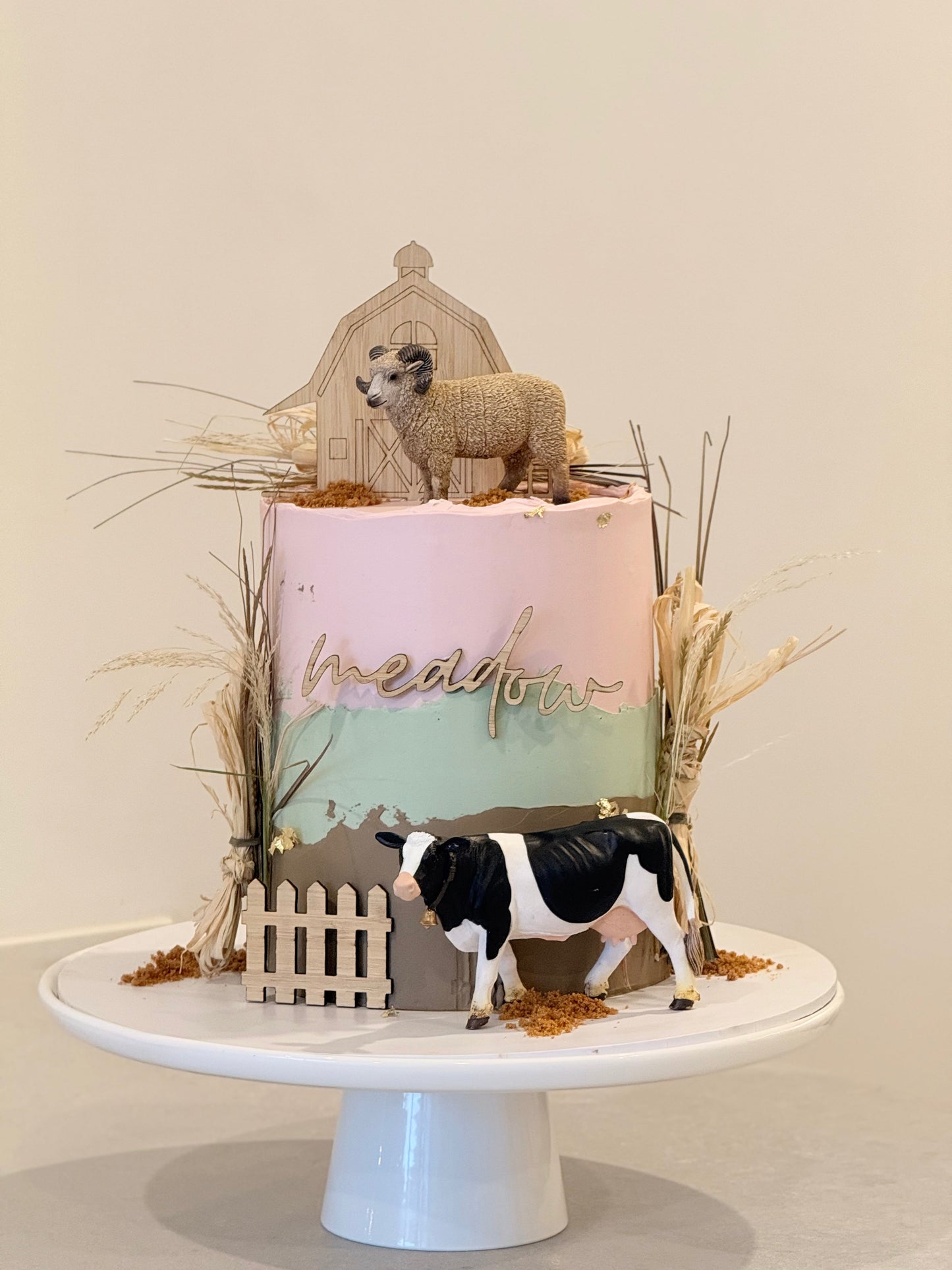Decorative cake with sheep and cow figurines on a white stand against a beige background