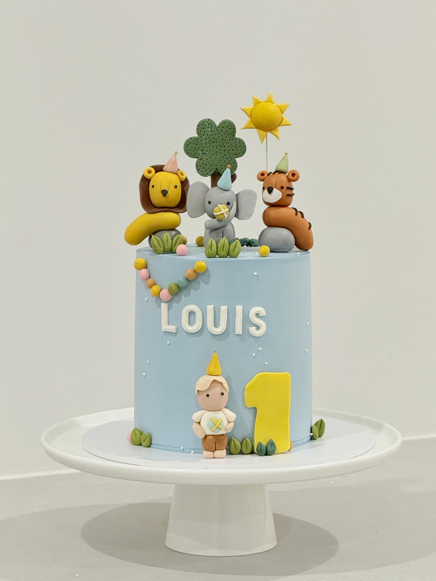 Children's birthday cake with animal figurines and 'LOUIS 1' on a white background