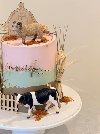 Decorative cake with sheep and cow figurines on a white surface
