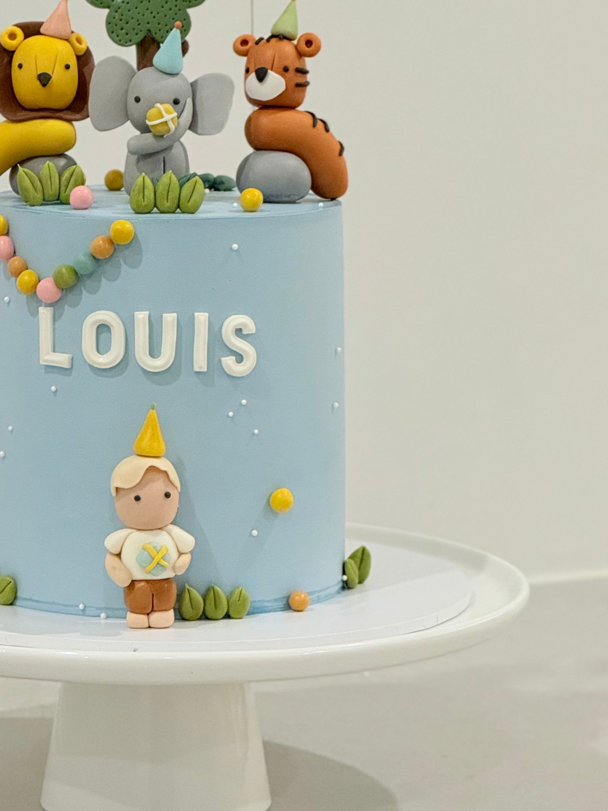 Children's birthday cake with animal figurines and 'LOUIS' on a light blue background