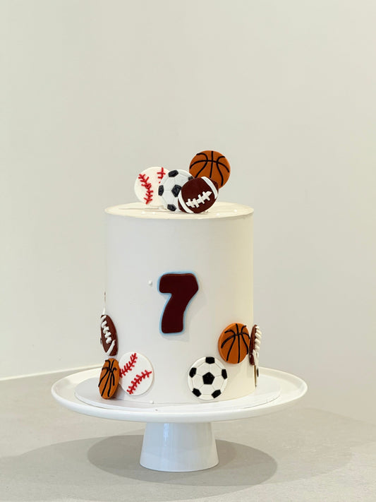 Cake with sports-themed decorations on a white stand against a light gray background