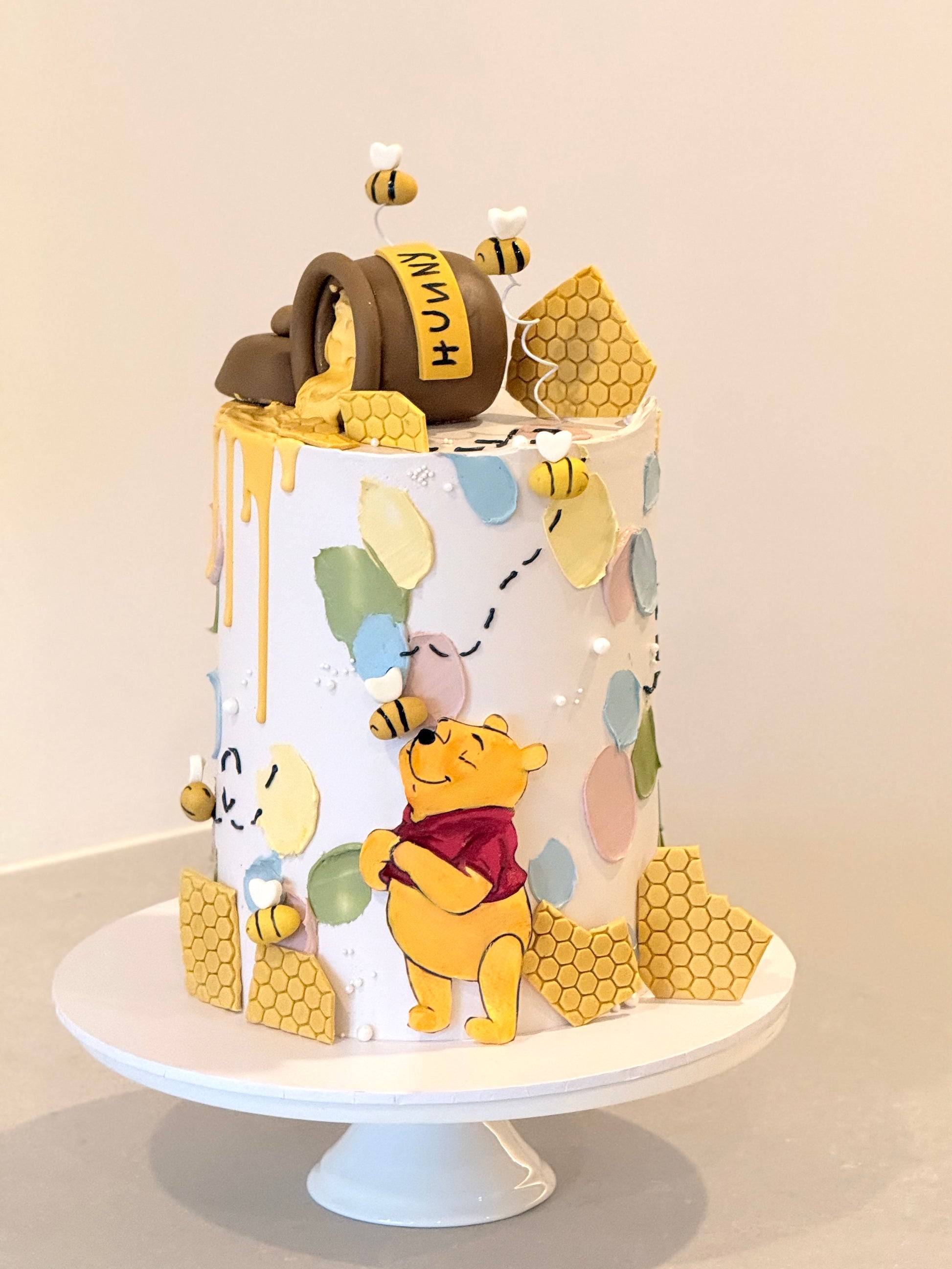 Cake decorated with Winnie the Pooh and honeycomb elements on a white stand.