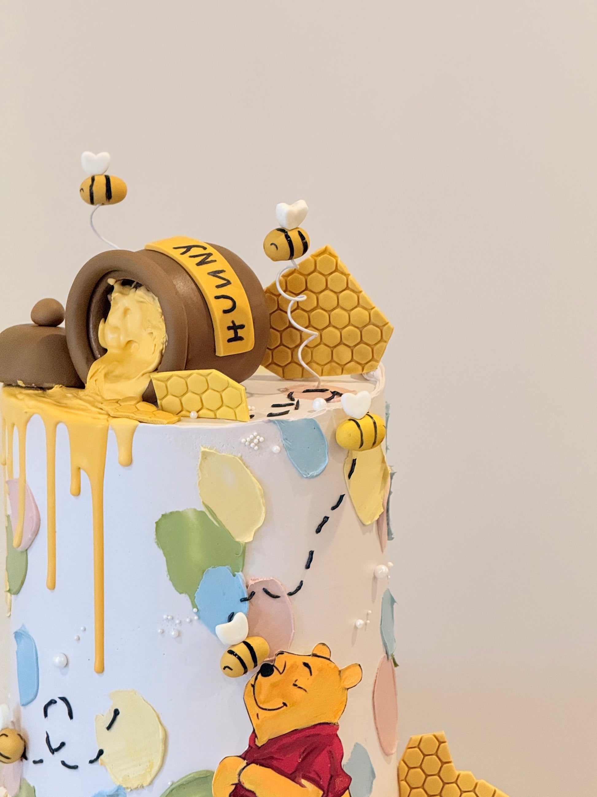 Children's birthday cake with Winnie the Pooh and honeycomb decorations on a light gray background